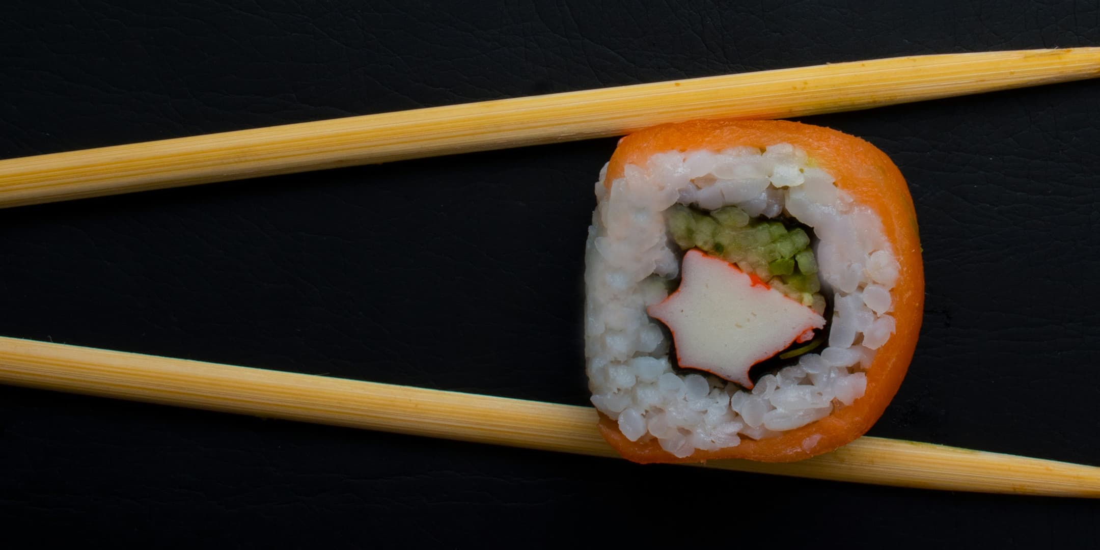 Piece of California sushi being held by chopsticks