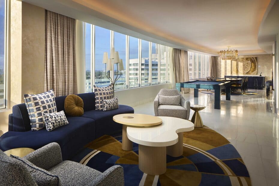 Spacious luxury suite living area with blue seating, large windows, a pool table, and a dining area.